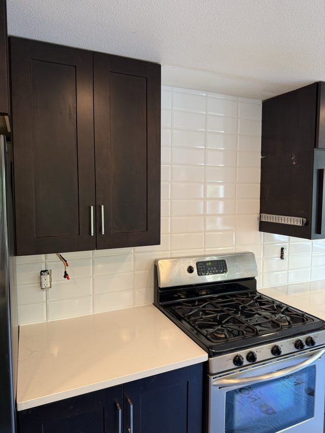 kitchen with dark cabinets, gas range, white subway backsplash