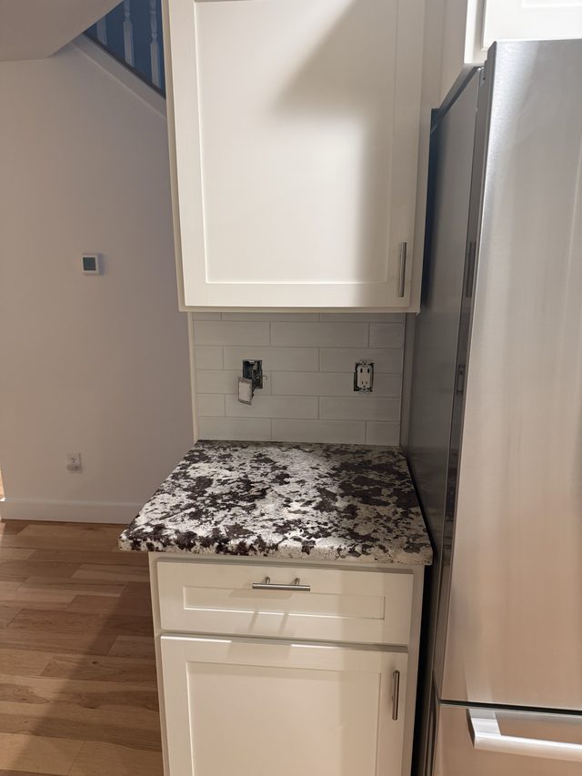 white cabinet, granite counter, subway backsplash beside fridge