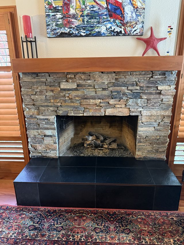 stacked stone fireplace with black tile hearth in living area